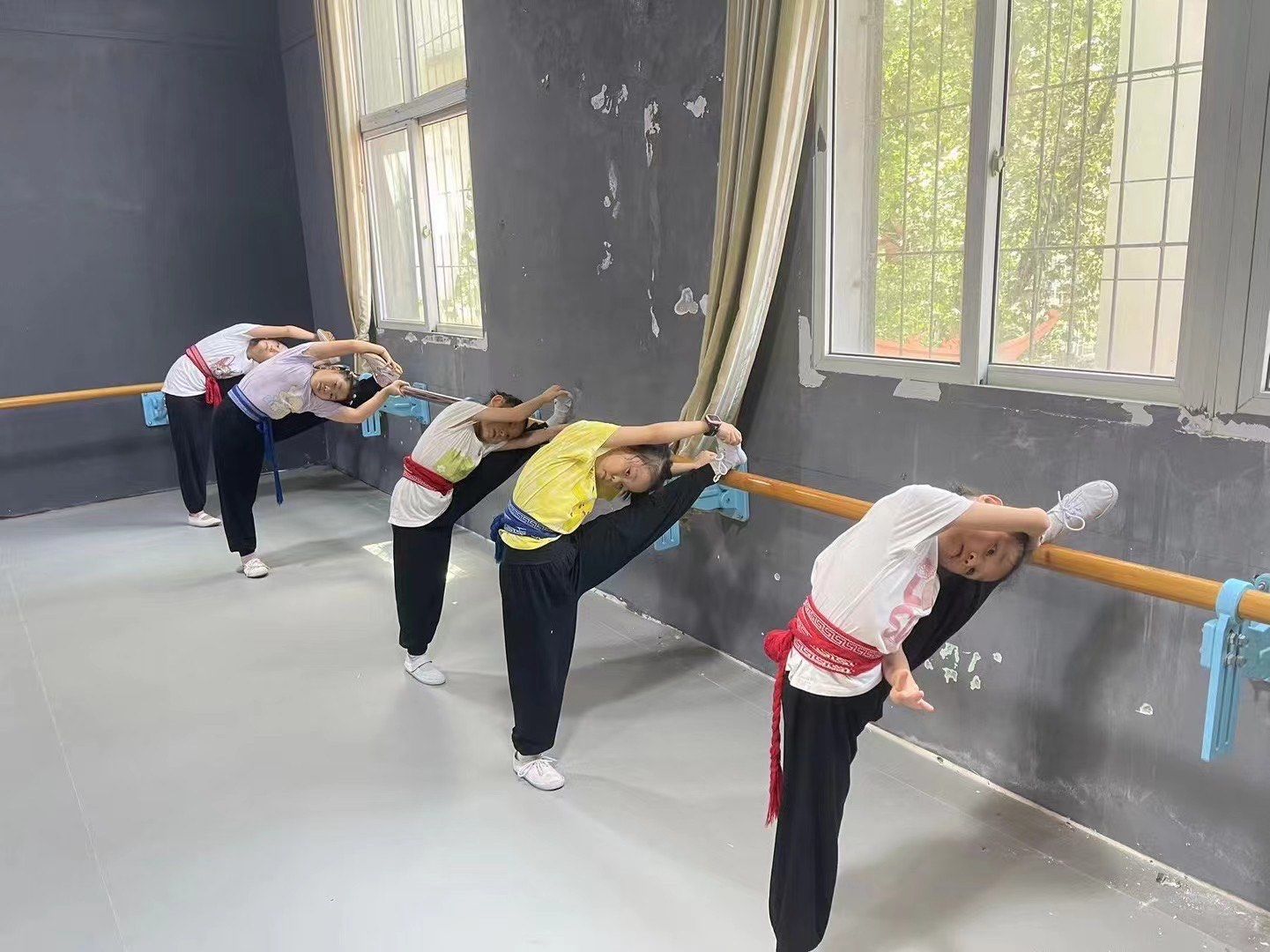 图中,孩子们身着练功服,腰系彩绸,在老师的指导下进行基本功练习